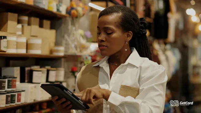 Mulher negra empreendedora usando tablet para gerir estoque em loja de produtos artesanais e velas.