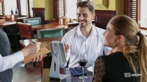 Homem sorrindo em restaurante com amigos e garçom.