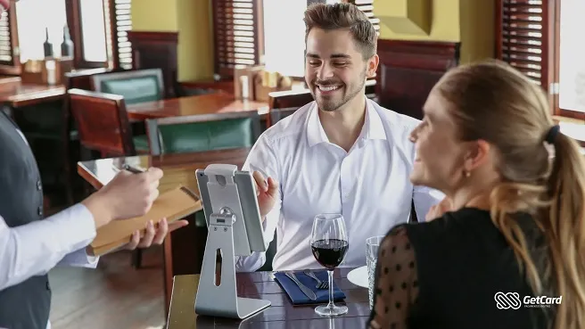 Homem sorrindo em restaurante com amigos e garçom.