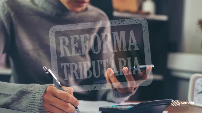 Pessoa escrevendo em documentos ao lado de uma calculadora, com carimbo digital sobreposto escrito 'Reforma Tributária'.
