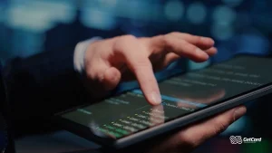 Close de mãos interagindo com tela de tablet exibindo códigos e dados digitais em ambiente futurista.