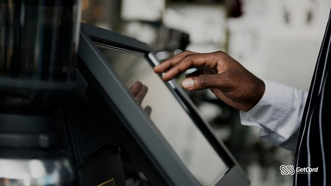 Mão de pele retinta operando tela touchscreen de um sistema de vendas em um estabelecimento comercial.
