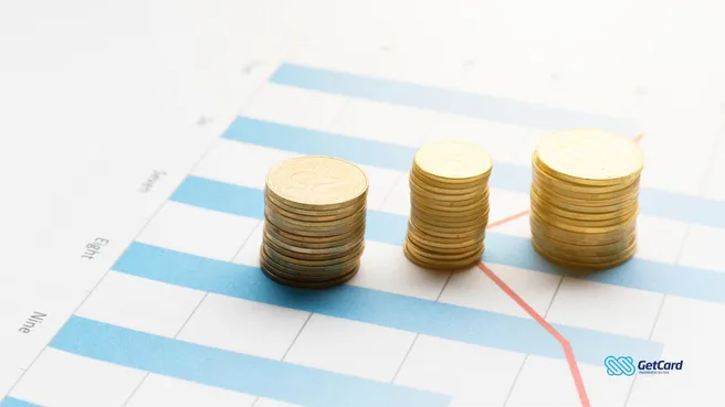 Três pilhas crescentes de moedas douradas sobre gráfico de barras azul e linha de tendência.