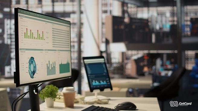 imagensBlog4 Monitor exibindo dashboard com gráficos financeiros e métricas em escritório moderno com tablet e café sobre a mesa.
