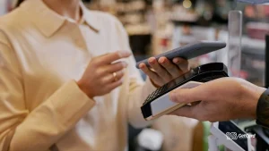 Cliente realizando pagamento por aproximação com smartphone em maquininha de cartão no caixa de uma loja.