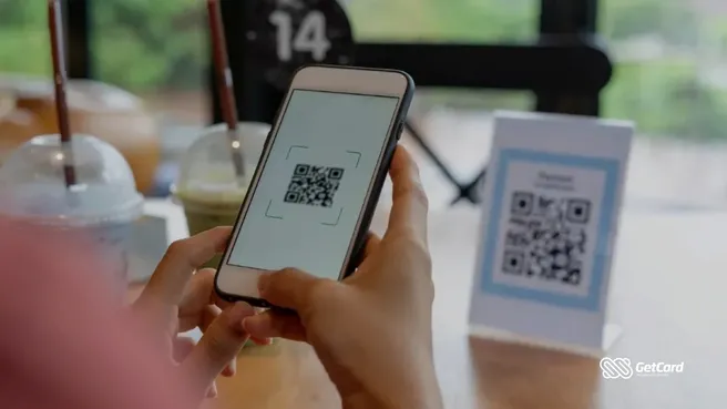 Pessoa usando smartphone para escanear QR Code de pagamento sobre mesa de cafeteria.